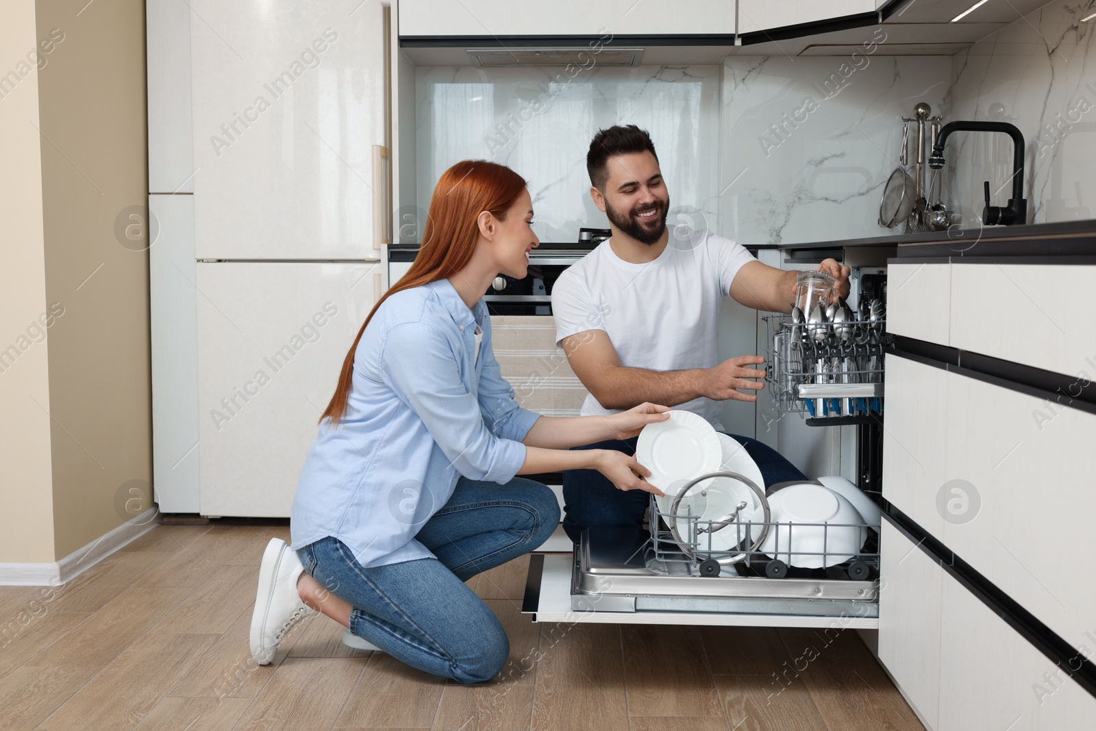 Photo of Happy couple loading dishwasher with plates in kitchen