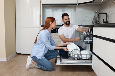 Photo of Happy couple loading dishwasher with plates in kitchen