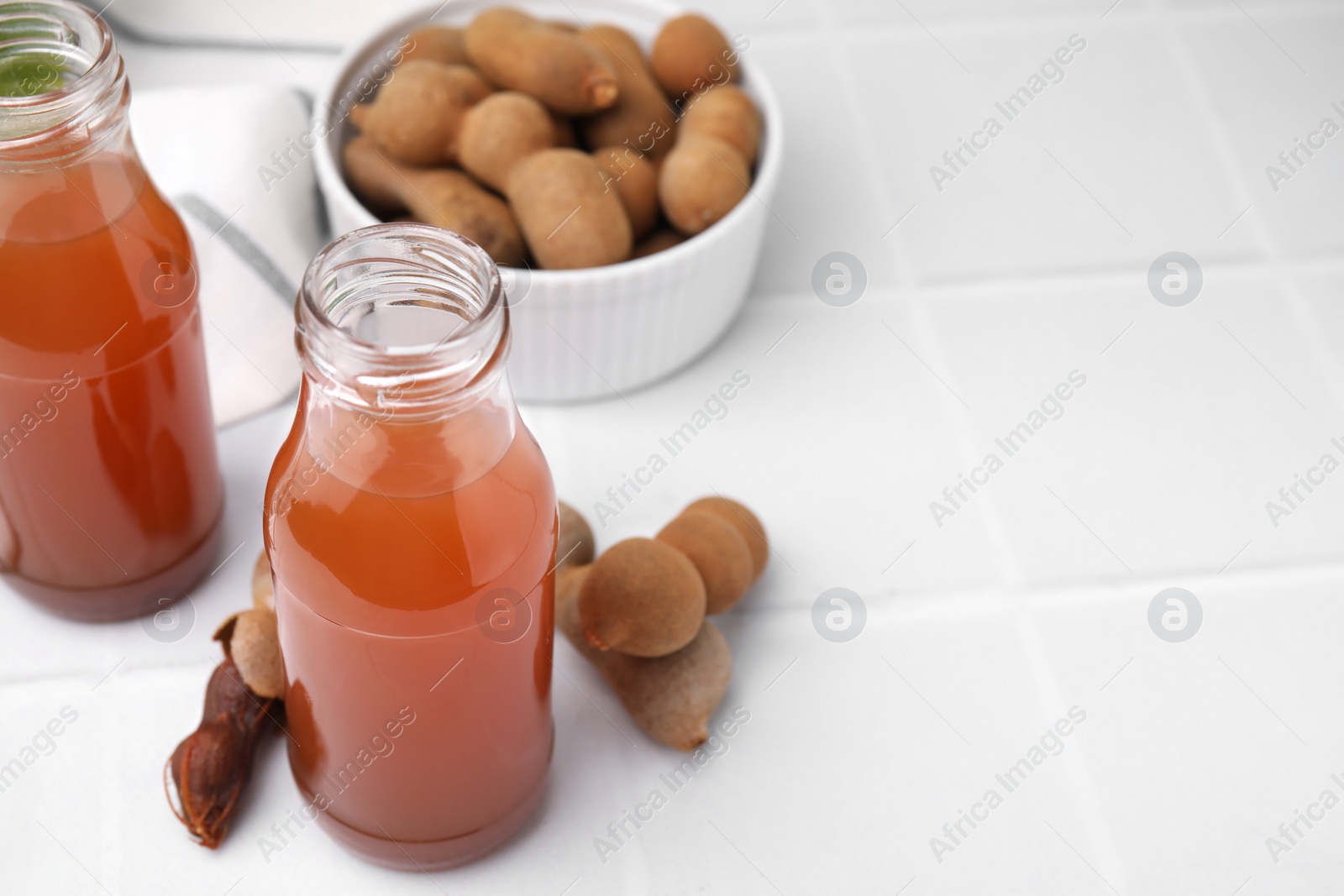 Photo of Tamarind juice and fresh fruits on white tiled table, space for text