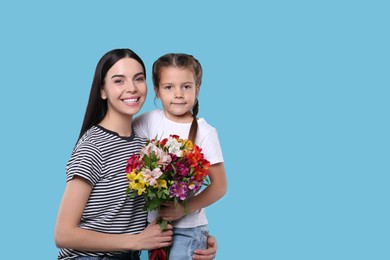 Happy woman with her daughter and bouquet of beautiful flowers on light blue background, space for text. Mother's day celebration