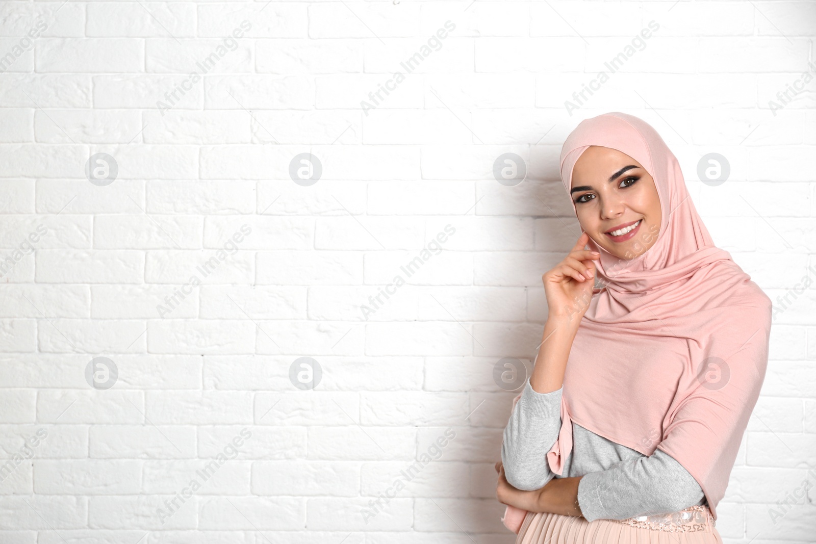 Photo of Portrait of young Muslim woman in hijab against brick wall. Space for text