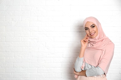 Portrait of young Muslim woman in hijab against brick wall. Space for text