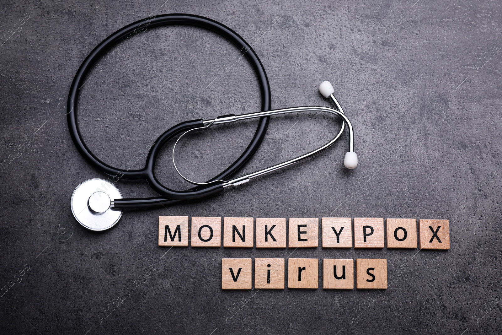 Photo of Words Monkeypox Virus made of wooden squares and stethoscope on grey table, flat lay