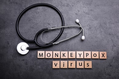 Words Monkeypox Virus made of wooden squares and stethoscope on grey table, flat lay