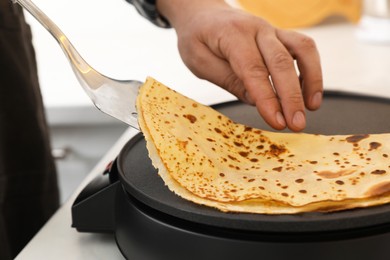 Man cooking delicious crepe on electric pancake maker at table, closeup