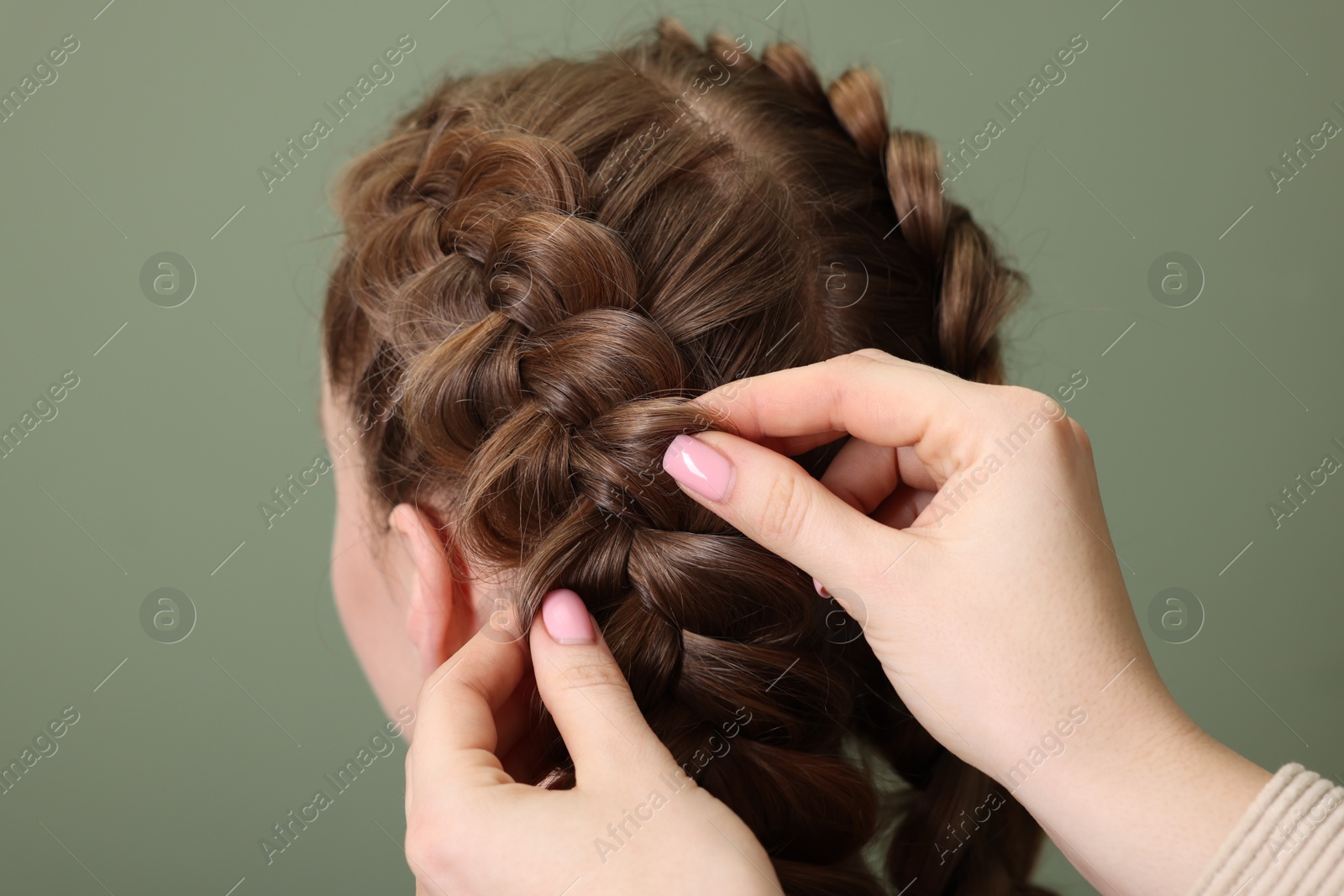 Photo of Professional stylist braiding woman's hair on olive background, closeup