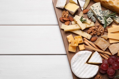 Cheese plate with grapes and nuts on white wooden table, top view. Space for text