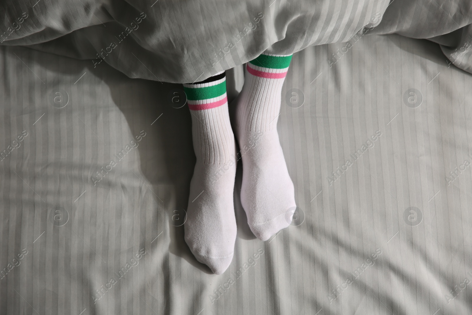 Photo of Woman wearing socks under blanket in bed, top view