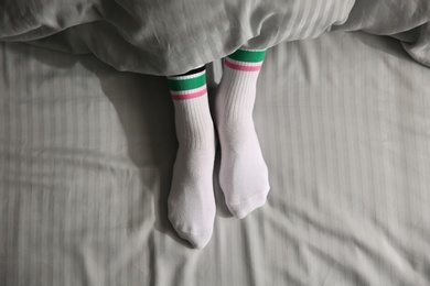 Woman wearing socks under blanket in bed, top view