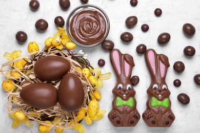 Flat lay composition with chocolate Easter bunnies, eggs and candies on white textured table