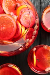 Photo of Glasses and bowl of delicious aromatic punch drink on black wooden table, flat lay