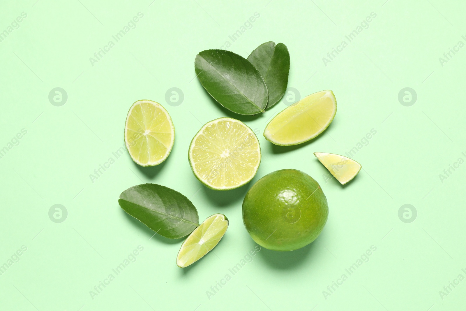 Photo of Whole and cut fresh ripe limes with leaves on light green background, flat lay