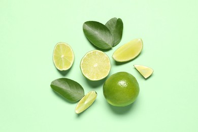 Photo of Whole and cut fresh ripe limes with leaves on light green background, flat lay