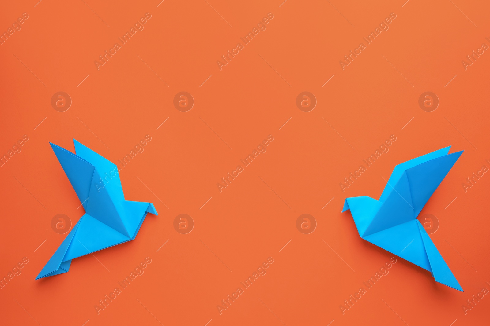 Photo of Beautiful light blue origami birds on orange background, flat lay. Space for text