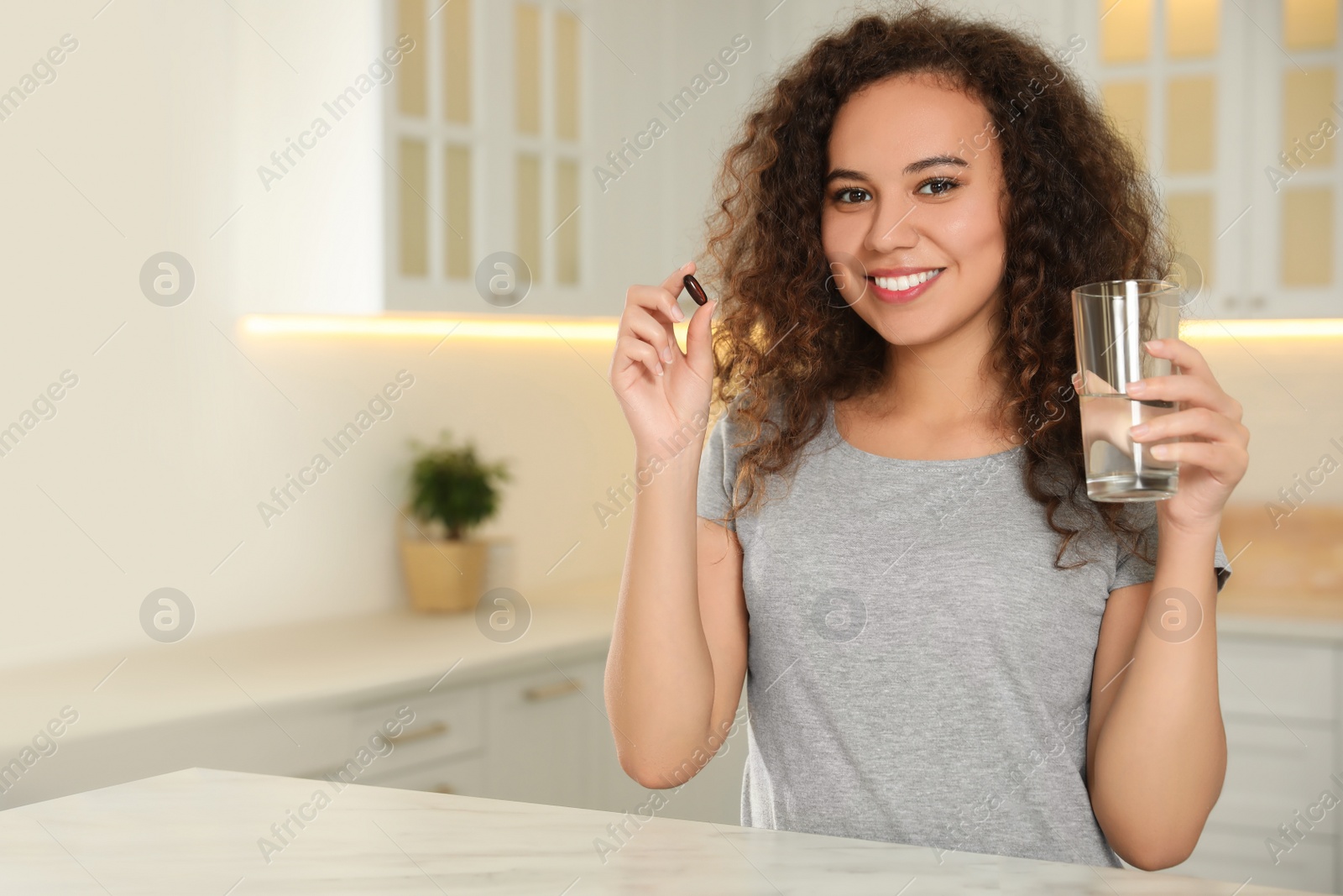 Photo of African-American woman with glass of water and vitamin capsule in kitchen. Space for text