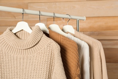 Photo of Collection of warm sweaters hanging on rack against wooden background