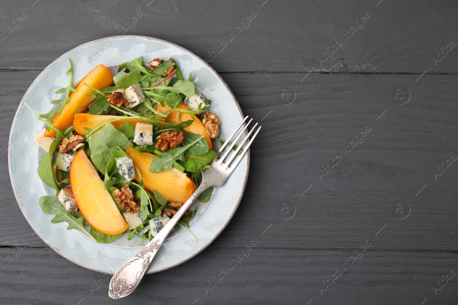 Photo of Tasty salad with persimmon, blue cheese and walnuts served on grey wooden table, top view. Space for text