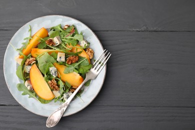 Photo of Tasty salad with persimmon, blue cheese and walnuts served on grey wooden table, top view. Space for text