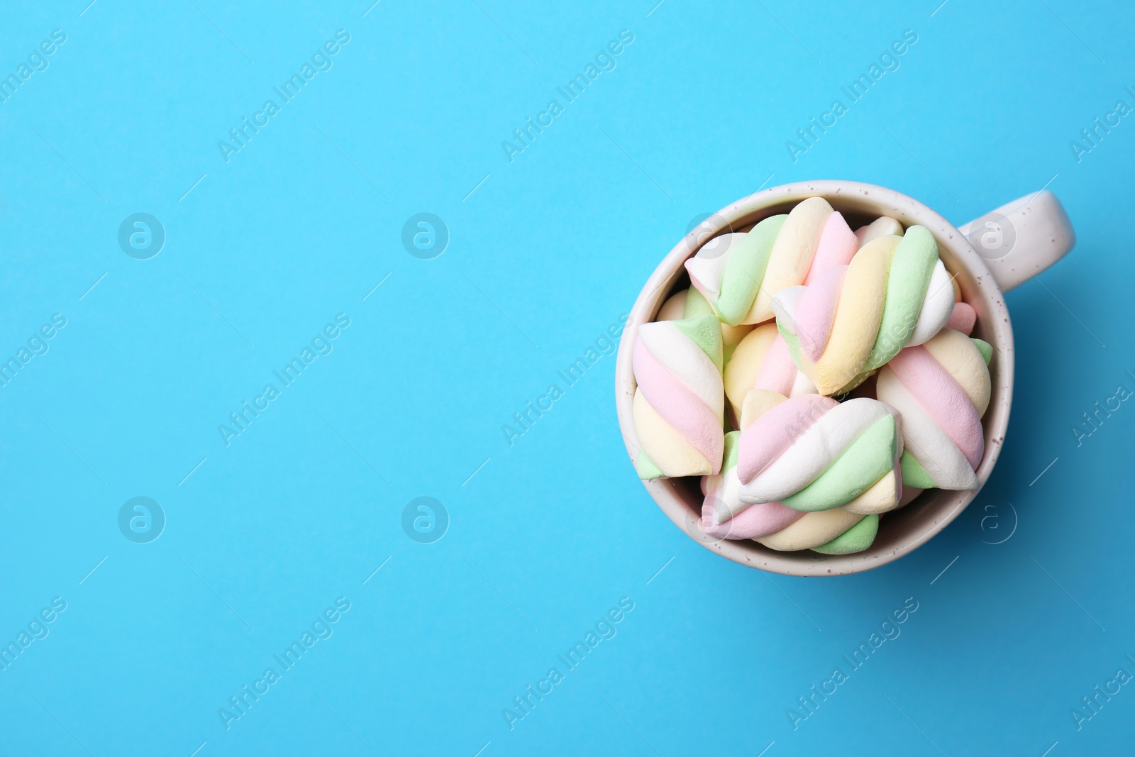 Photo of Delicious colorful marshmallows in cup on light blue background, top view. Space for text