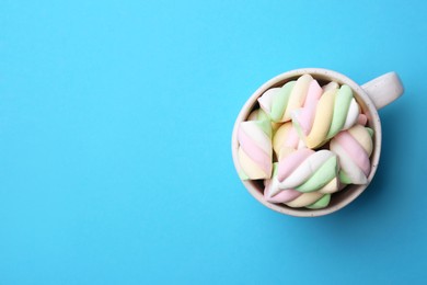 Delicious colorful marshmallows in cup on light blue background, top view. Space for text