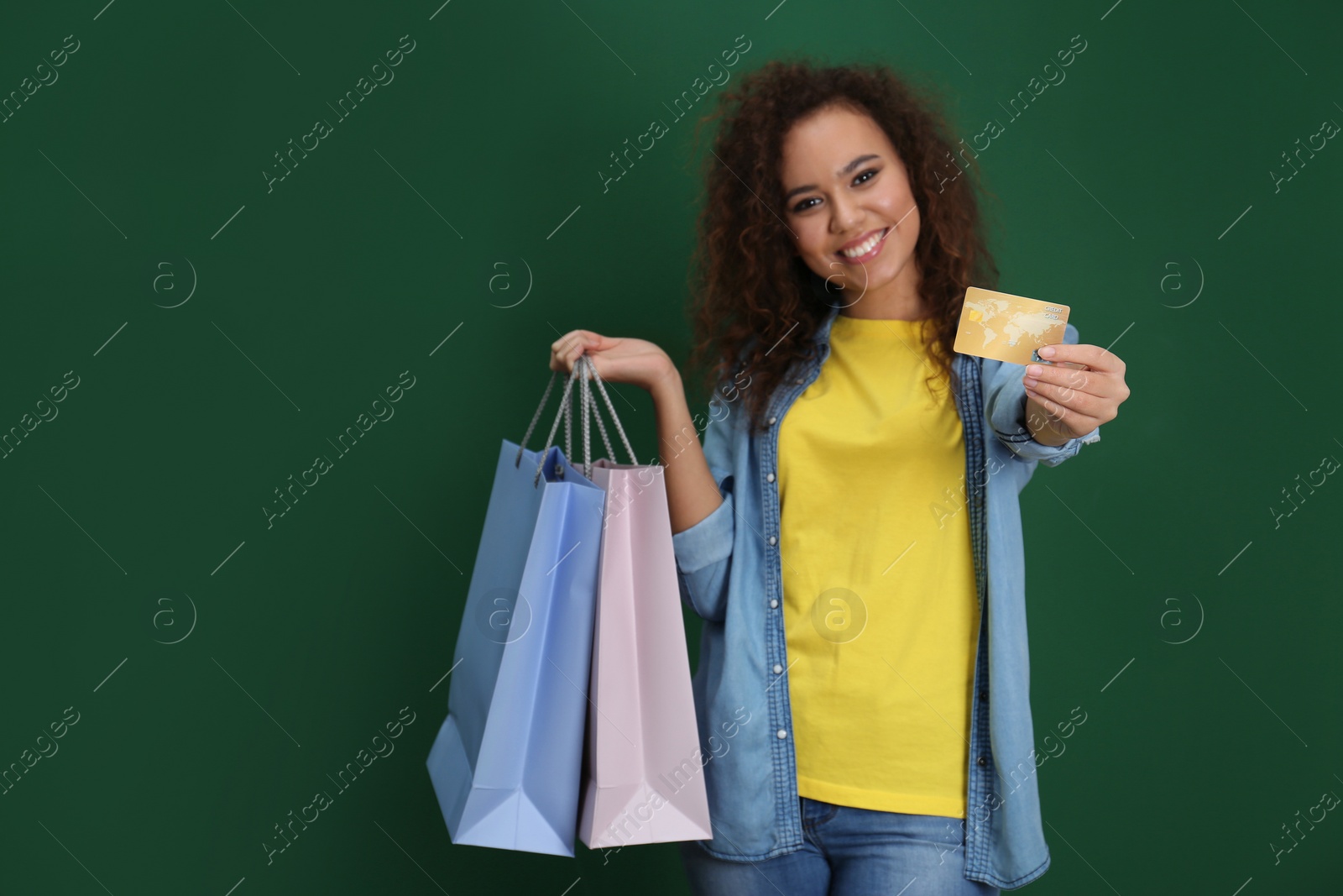 Photo of Young African-American woman with credit card and shopping bags on color background, space for text. Spending money