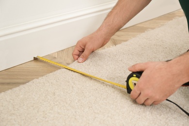 Photo of Worker with measuring tape installing new carpet indoors, closeup