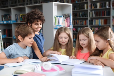 Group of happy little children reading books at table in library