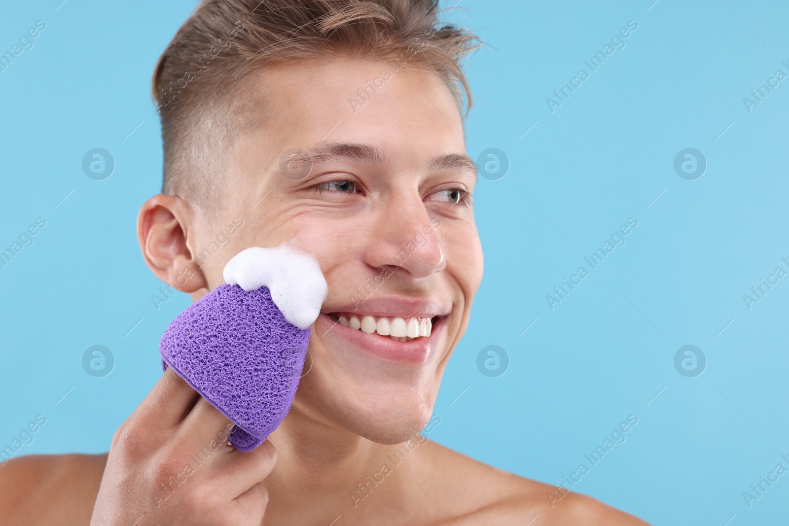 Photo of Happy young man washing his face with sponge on light blue background. Space for text