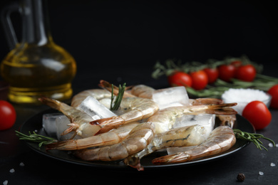 Photo of Fresh raw shrimps with rosemary and ice cubes on black table