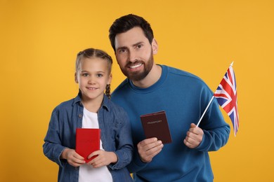 Immigration. Happy man with his daughter holding passports and flag of United Kingdom on orange background
