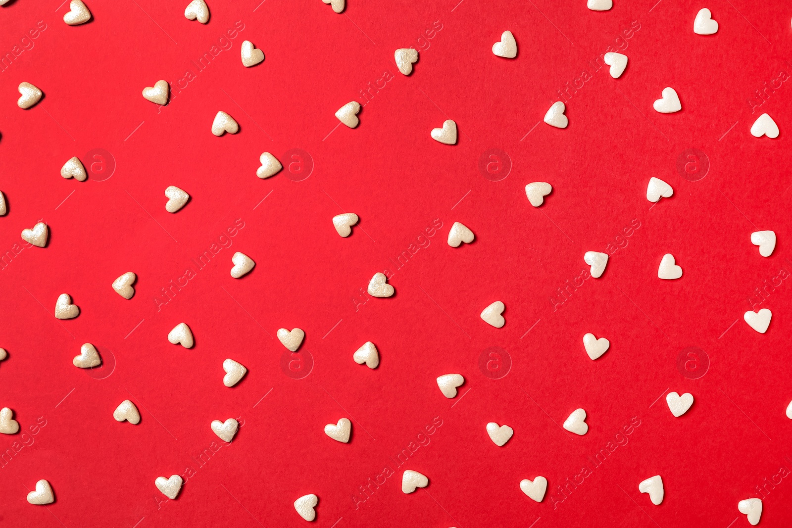 Photo of White heart shaped sprinkles on red background, flat lay