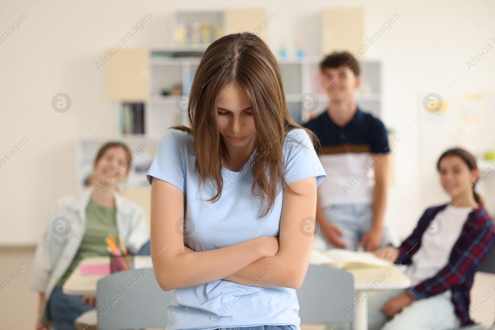 Photo of Teen problems. Lonely girl standing separately from other students in classroom