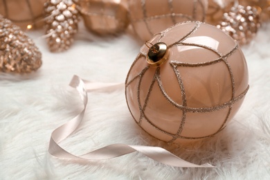 Photo of Beautiful Christmas tree bauble with ribbon on white faux fur, closeup