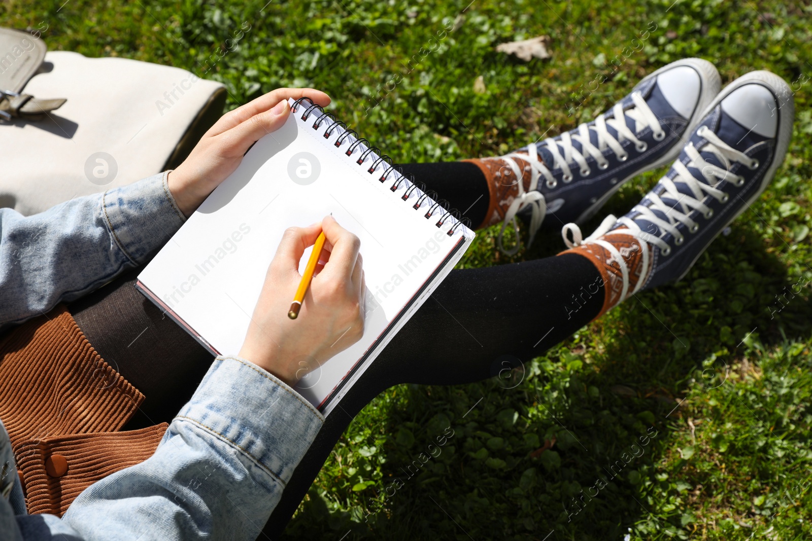 Photo of Woman drawing in sketchbook outdoors on green grass, closeup