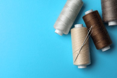 Photo of Different colorful sewing threads with needle on light blue background, flat lay. Space for text