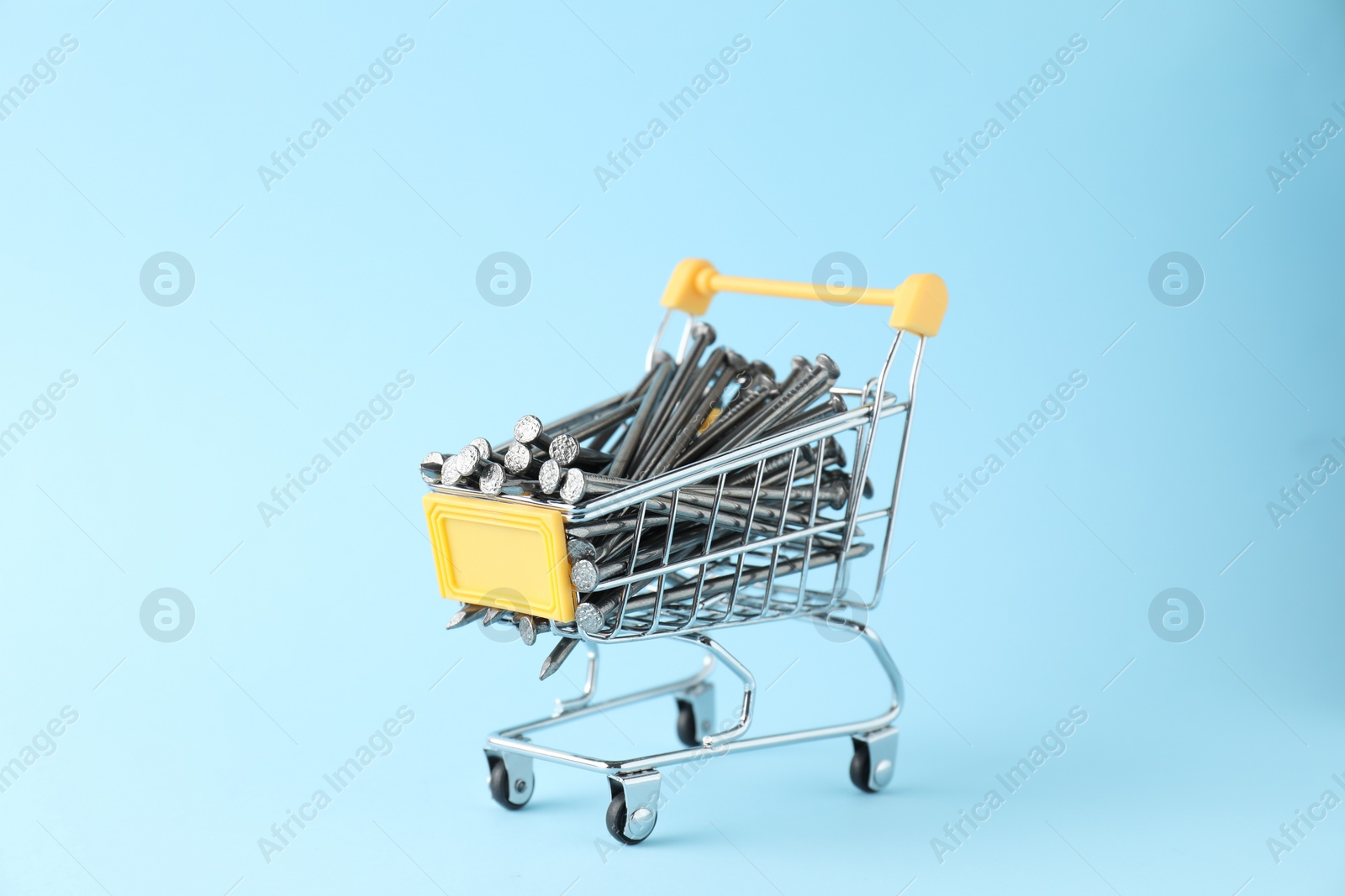 Photo of Metal nails in shopping cart on light blue background
