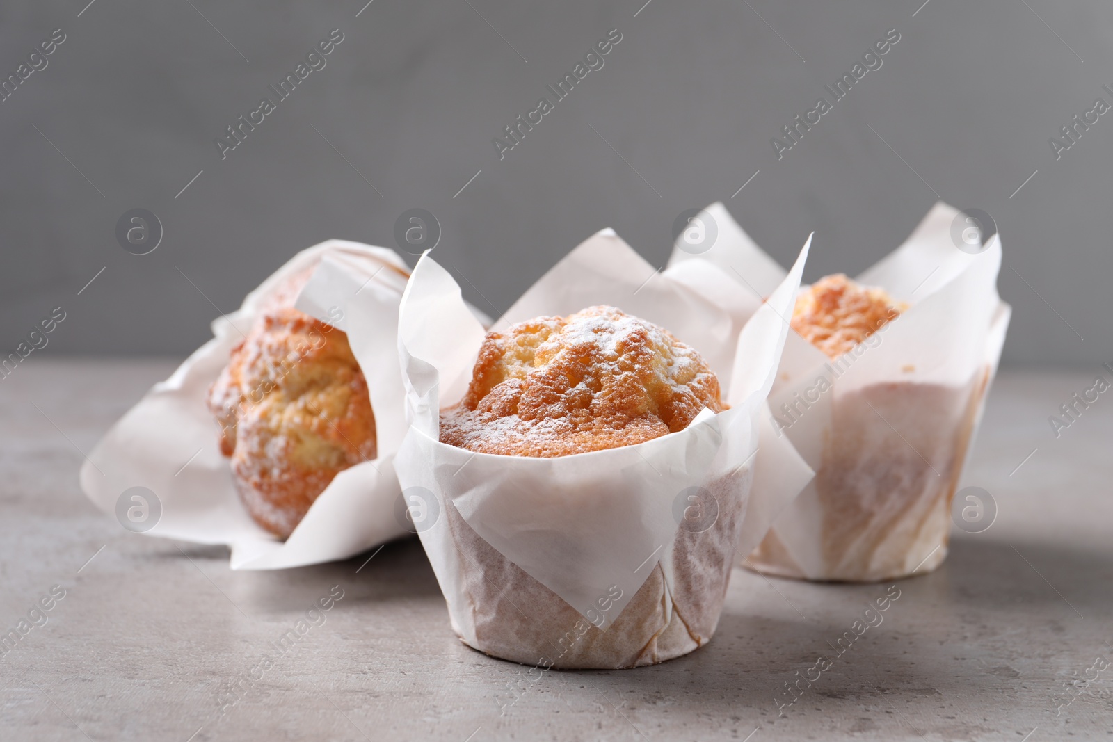 Photo of Delicious muffins with powdered sugar on grey table, closeup