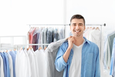 Photo of Young man holding hanger with jacket in plastic bag at dry-cleaner's