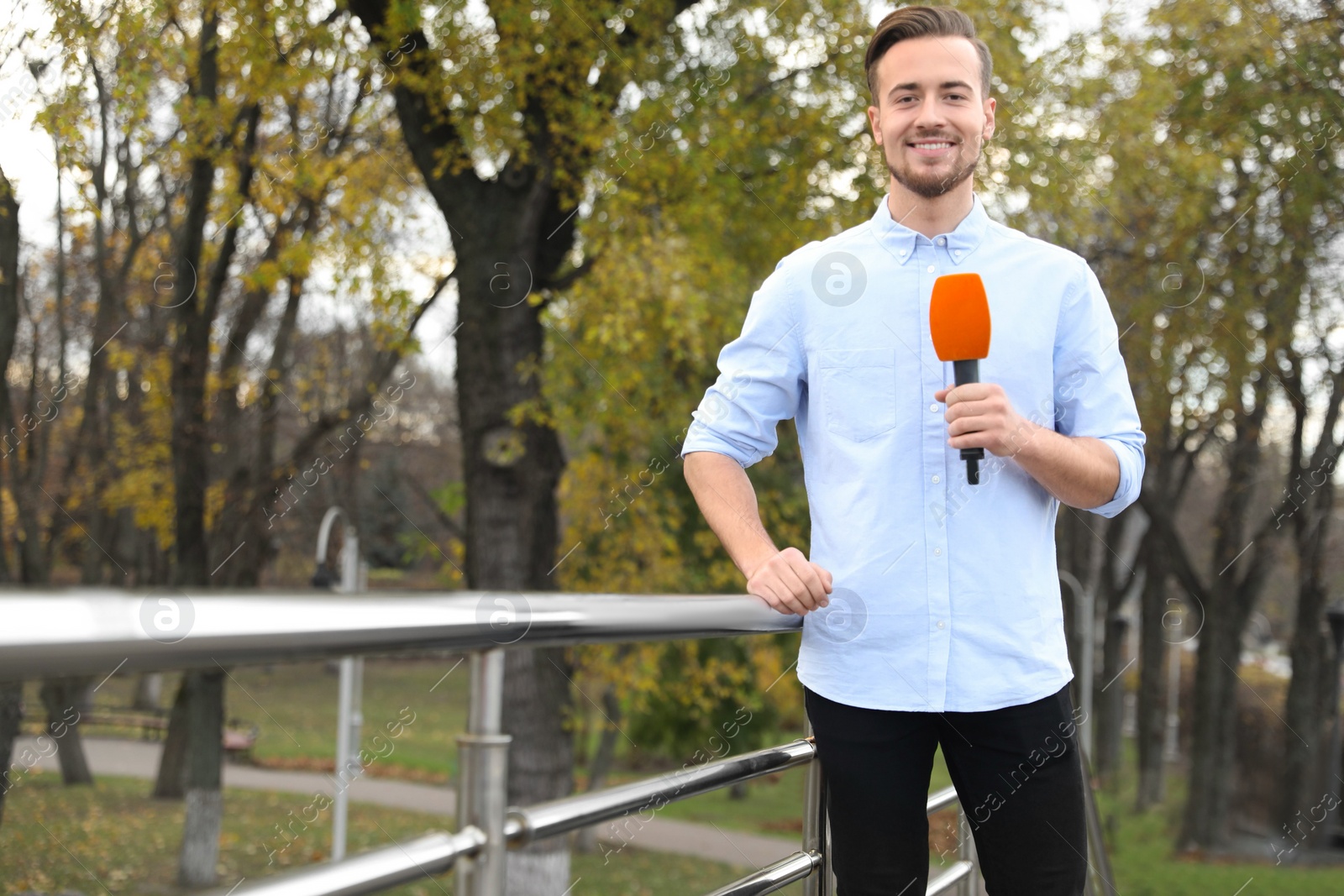 Photo of Young male journalist with microphone working in park. Space for text