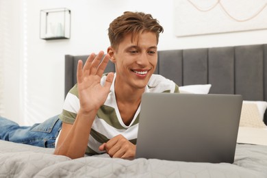 Photo of Happy young man having video chat via laptop on bed indoors