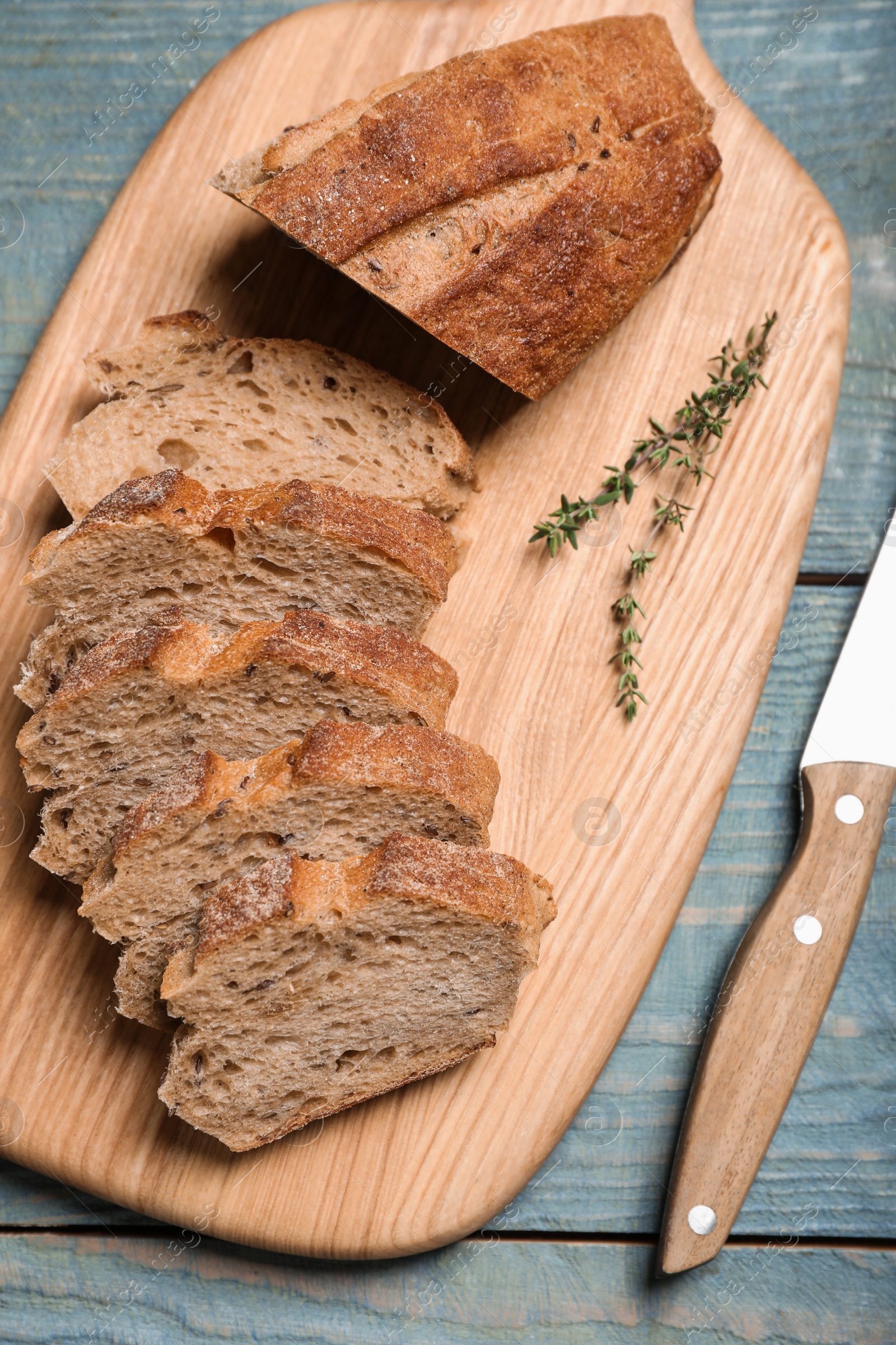 Photo of Cut buckwheat baguette with knife and thyme on light blue wooden table, flat lay