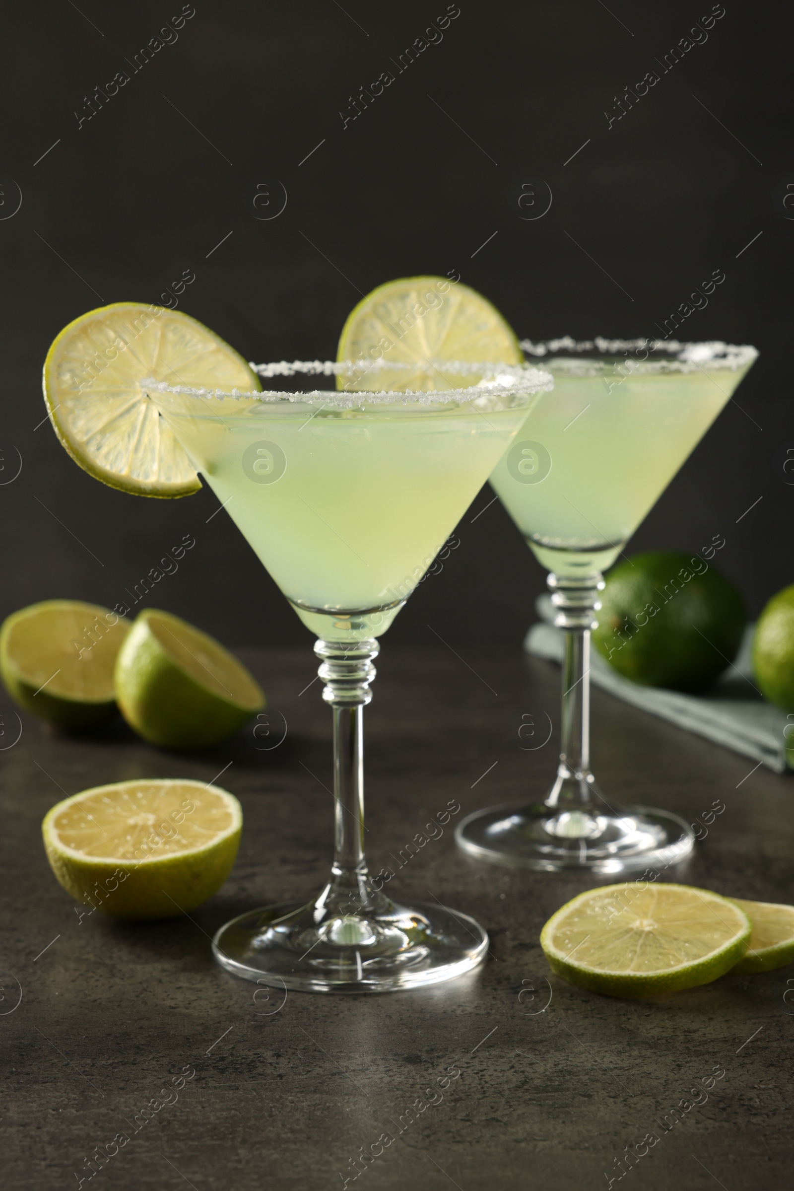 Photo of Delicious Margarita cocktail with ice cubes in glasses and limes on grey table