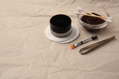 Photo of Eyebrow henna and tools on crumpled paper. Space for text