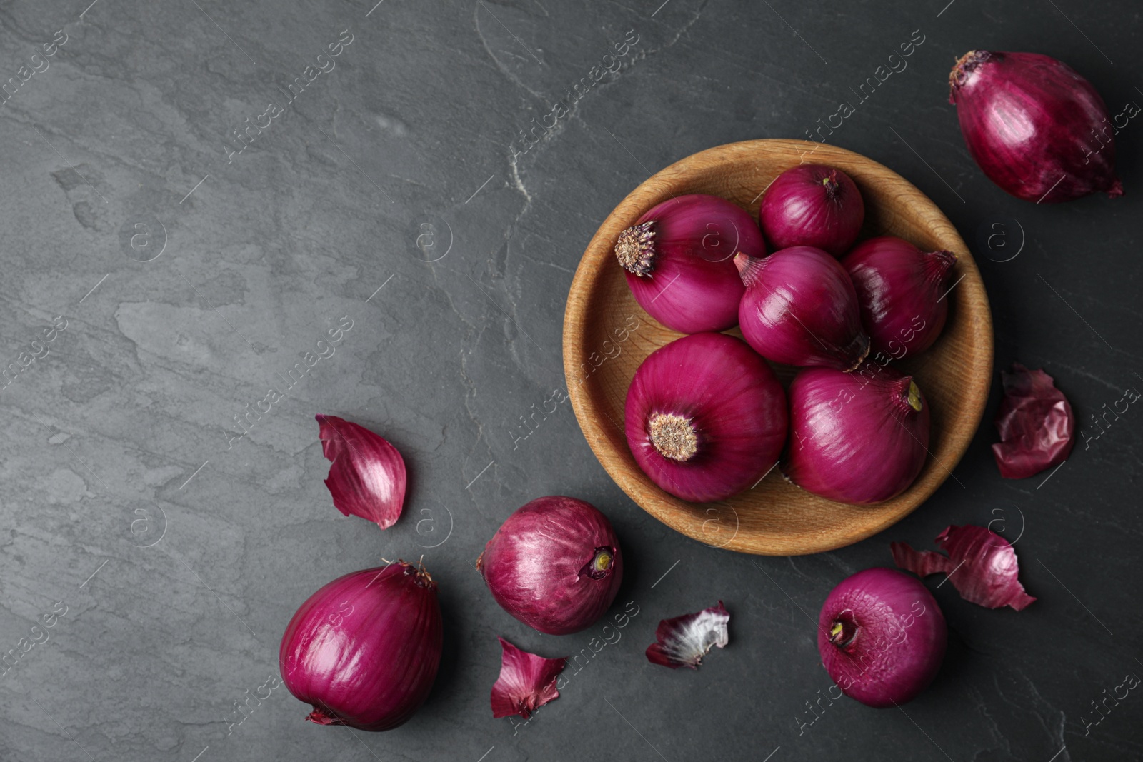 Photo of Ripe red onion bulbs and bowl on black table, flat lay. Space for text