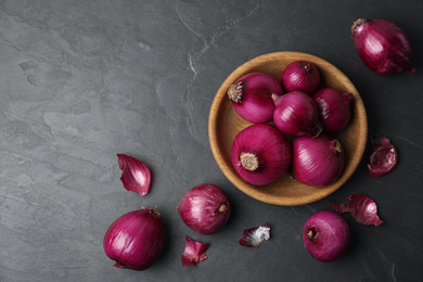 Photo of Ripe red onion bulbs and bowl on black table, flat lay. Space for text