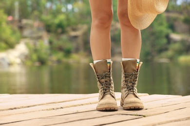 Photo of Young woman with hat on wooden pier near lake, focus on legs. Camping season