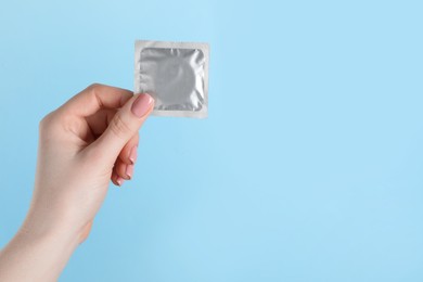 Woman holding condom on light blue background, closeup. Space for text