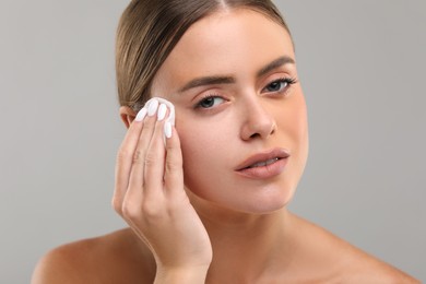 Beautiful woman removing makeup with cotton pad on grey background