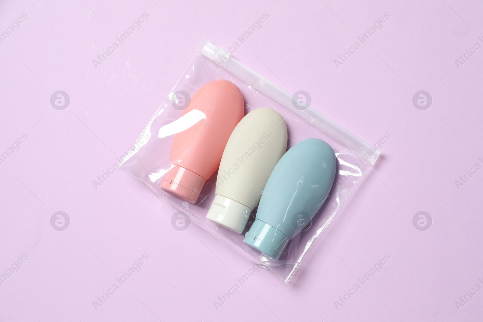 Photo of Cosmetic travel kit in plastic bag on violet background, top view