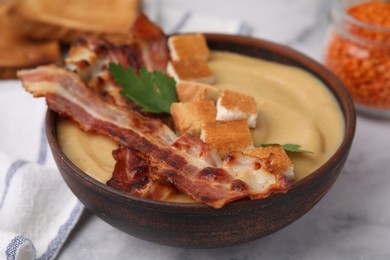 Photo of Delicious lentil soup with bacon and parsley in bowl on light table, closeup